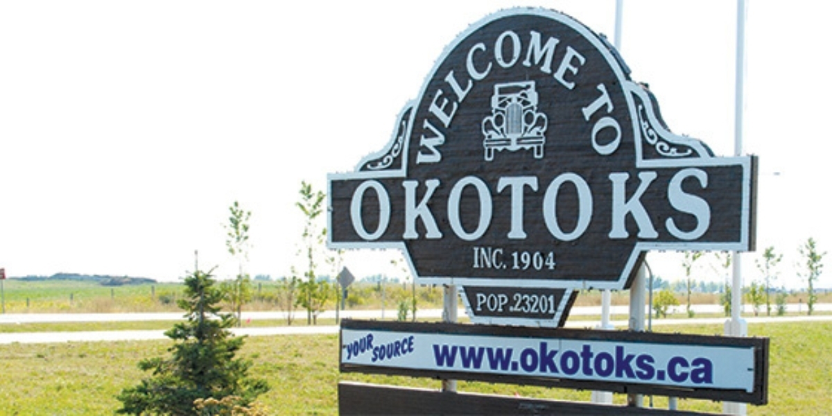 Okotoks' welcome sign with a road and green grass in the background