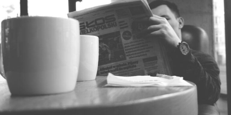 black and white image of a man reading the newspaper with coffee mugs on his table