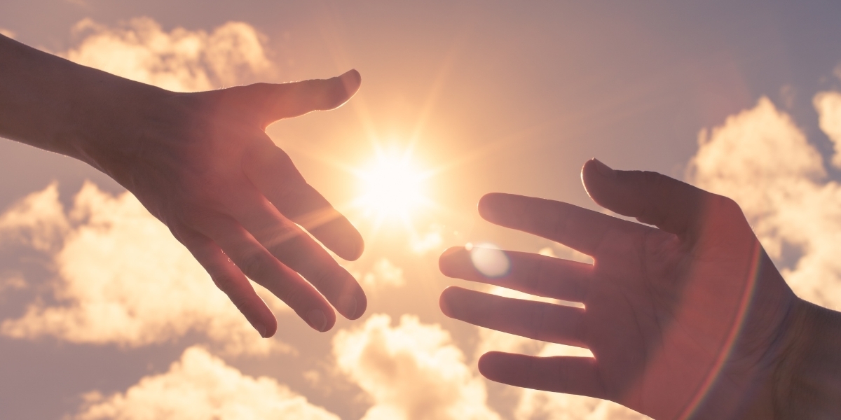 a photo of a hand reaching out to another hand with the sky and sun in the background