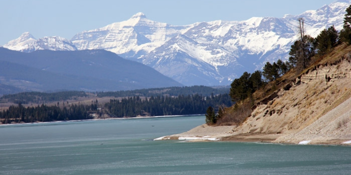 a picture of Ghost Lake with snow covered mountains and green forest in the background