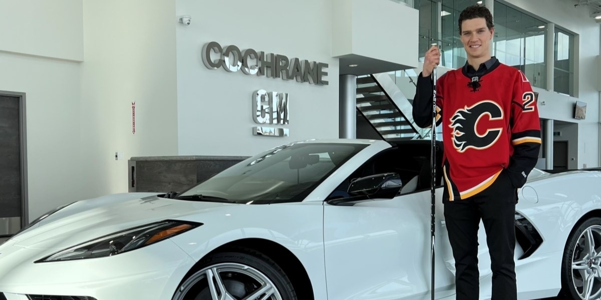 Mason Raymond wearing his Calgary Flames jersey holding a hockey stick and posing with a Corvette at his GM dealership
