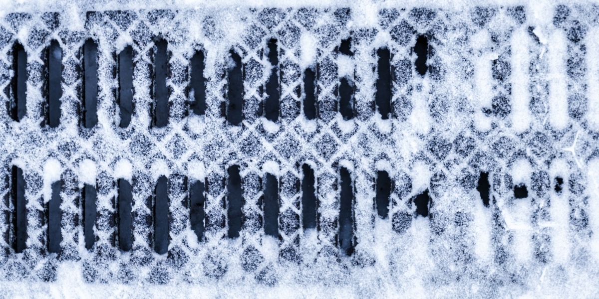 a photo of a sewer grate covered in snow and blocked by snow in some places