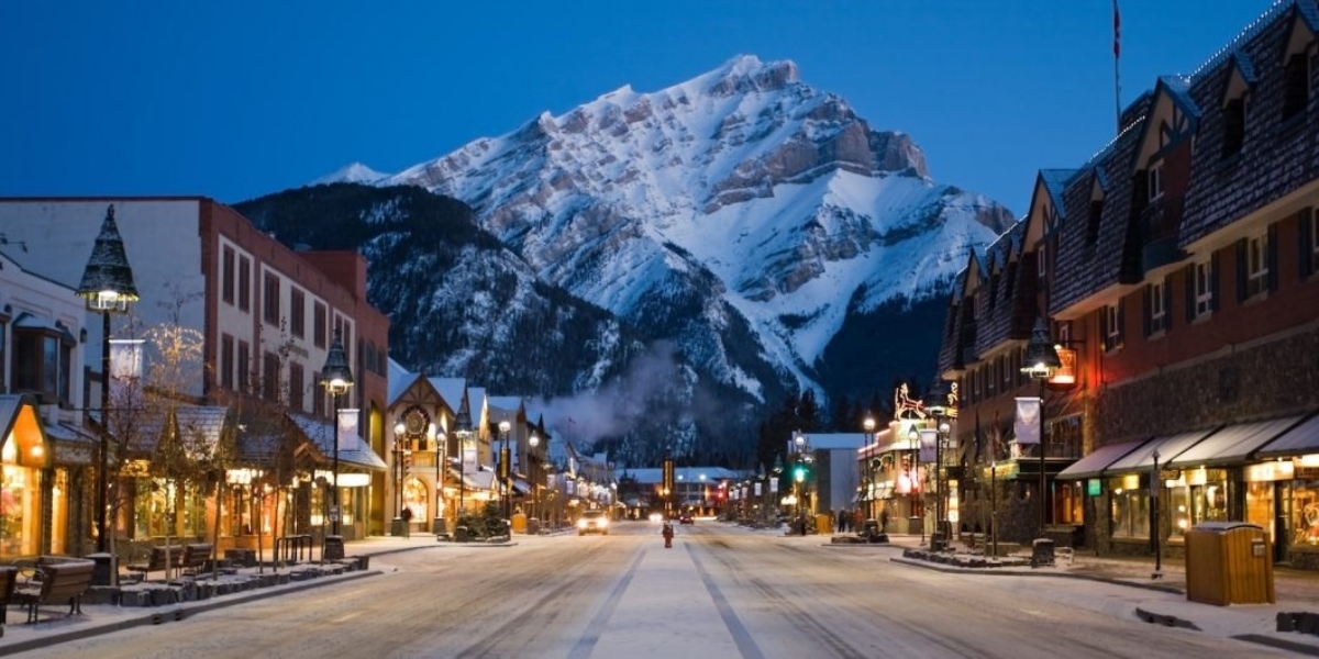 a picture of a busy Banff street during a winter evening with the Rockies in the background