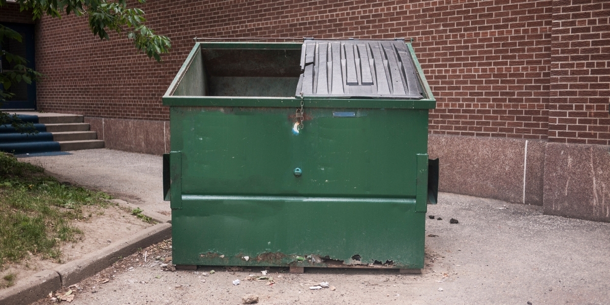 a generic photo of a green dumpster with a red brick building in the background