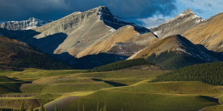 a beautiful landscape shot with the sun shining on the Rockies with vast green fields below
