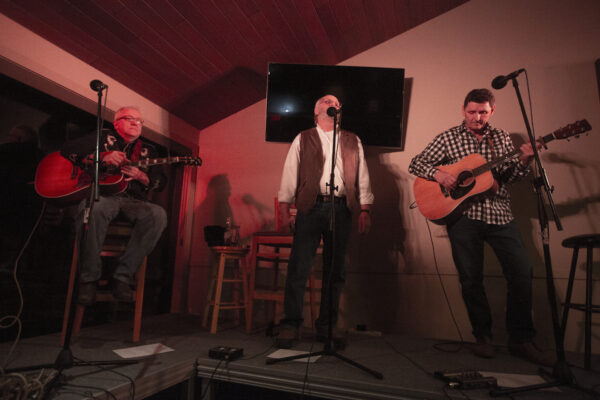a picture of Mike Petroff, Gord March and Pat Sullivan performing at the Songs for Shelter event playing guitar and singing into a microphone
