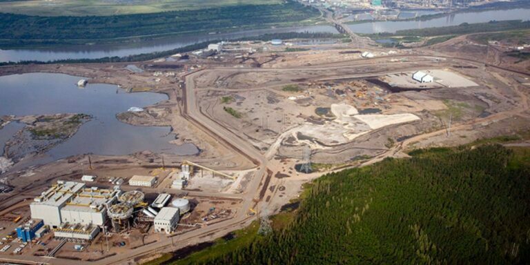 the barren landscape of suncors oil sands project in fort mcmurray surrounded by water and greenery