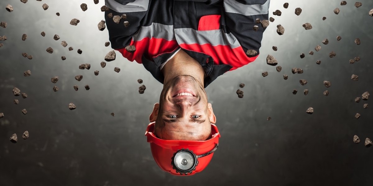 a coal miner wearing a hardhat flipped upside down with rocks falling from the top of the image