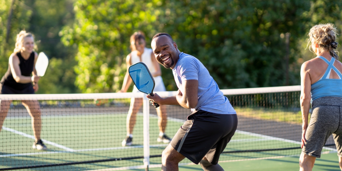 a picture of four people playing pickleball on a court smiling