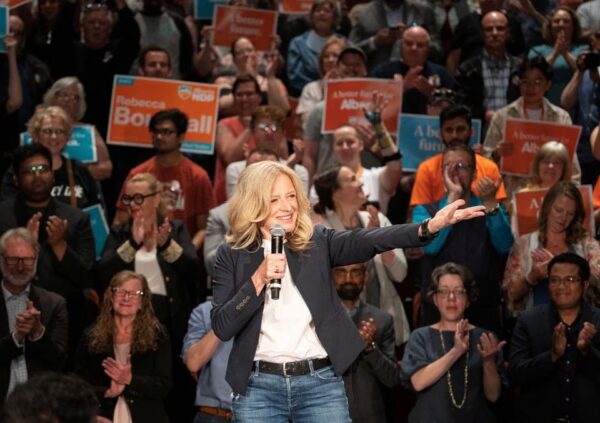 rachel notley at an ndp rally in calgary with supporters holding up orange ndp signs in the background