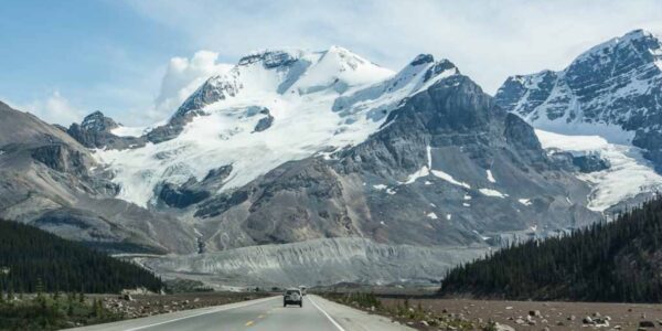 a photo of the icefields parkway with a car driving towards the mountains in the distance