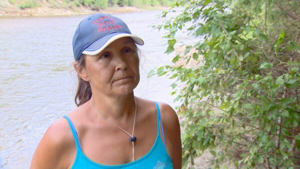 pembina river tubing owner cheryl harris in a blue top wearing a hat with the river behind her during an interview 