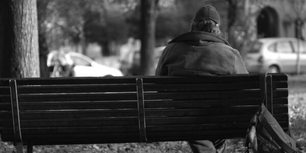 a black and white photo of a homeless man on a park bench taken from the back