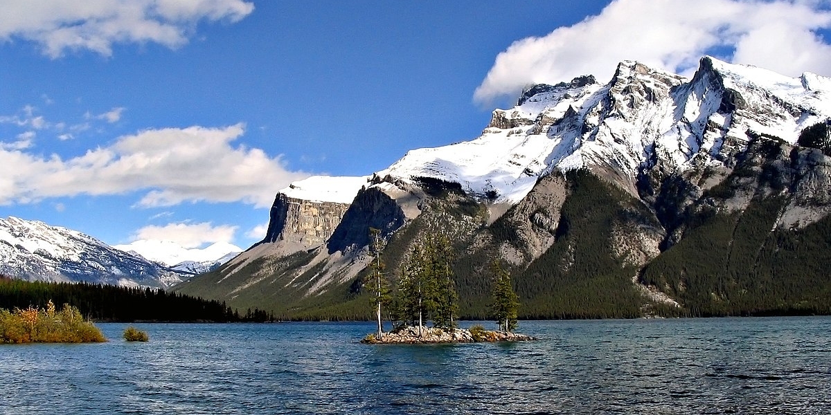 a beautiful photo of lake minnewanka with snow peaked rocky mountains in the background