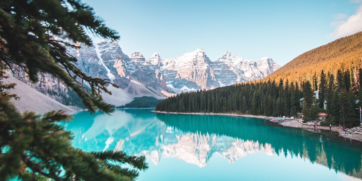 a photo of a crystal blue lake in alberta surrounded by snow covered mountains and green trees