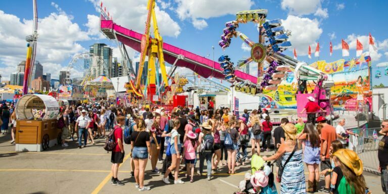 a colorful photo of the calgary stampede with many people walking around the grounds with fair rides in the background