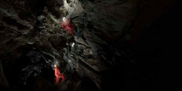 a dark photo of the eighteen metre rappel in rats nest cave with two explorers descending the narrow shaft illuminated from above