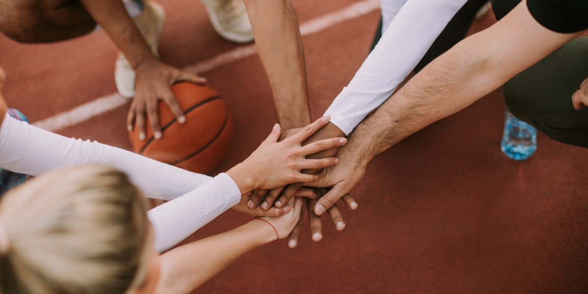 a diverse group of athletes laying their hands on top of each other to signify teamwork on a sports track with one man holding a basketball