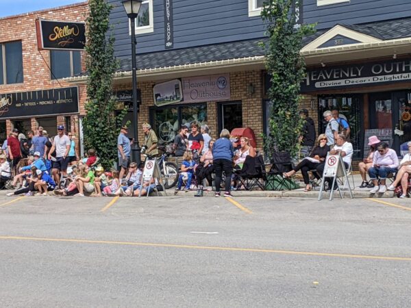 a crowd of people on main street standing and sitting in lawn chairs in front of outlet shops