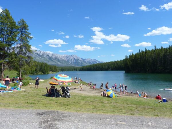 a crowd of people enjoying the sun and calm waters of johnson lake with blue skies and clouds above with distant mountains 