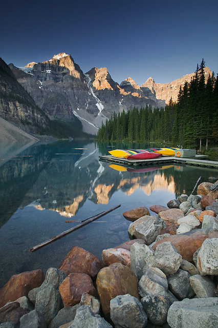 Photo of Moraine Lake at sunrise with canoes in the foreground.