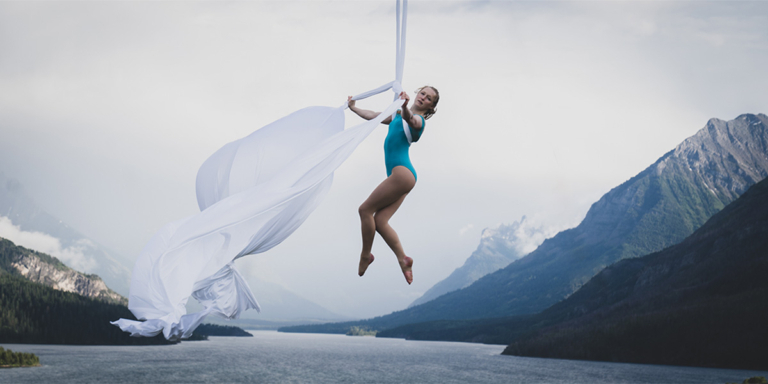 Image of aerialist performing above a lake with mountains in the background