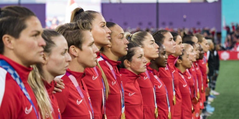 the canada womens national soccer team wearing their red uniforms with gold medals around their neck