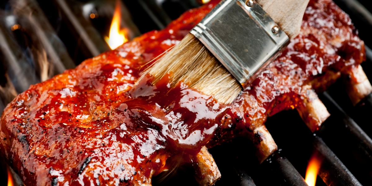 a rack of ribs on a grill being lathered with sauce