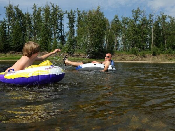 a man and his son tubing on mcleod river with forest in the background