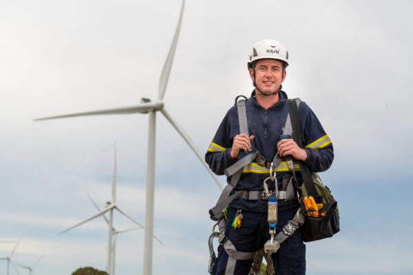 a photo of a wind turbine technician equipped with harnesses and a hardhat with wind turbines in the background