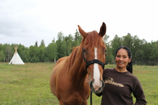a woman posing for a photo with her horse with a forest in the background