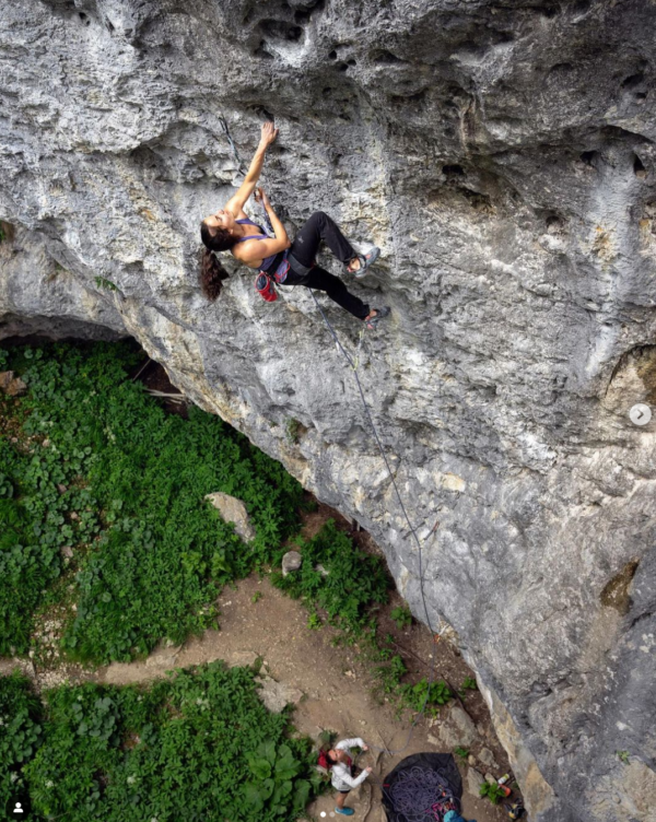 becca frangos scaling a steep wall with greenery below her