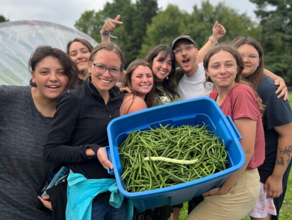 Students holding a plastic bin full of freshly harvested beans from a garden