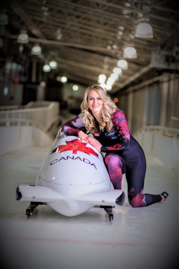 Woman posing with a bobsled on an indoor bobsled track
