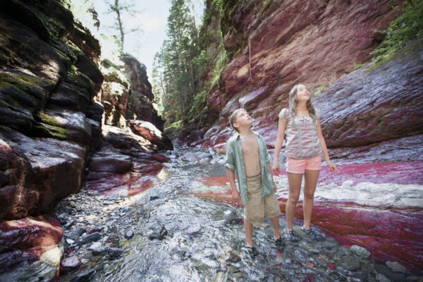 two children wading in a creek and gazing up at the colourful, red and white walls of Red Rock Canyon