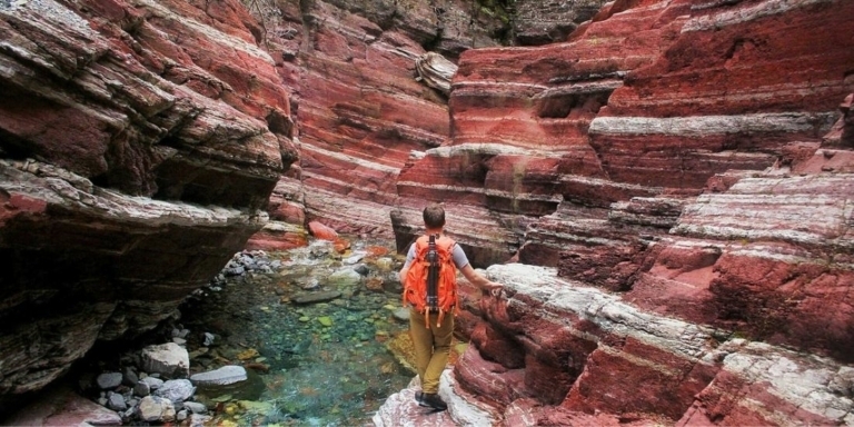 Backpacker in a canyon that has red and white stripped rock walls
