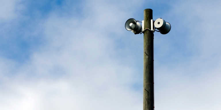 Loadspeakers mounted on a post photographed against a blue sky with clouds