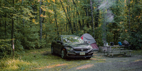 Car and tent in forested campground