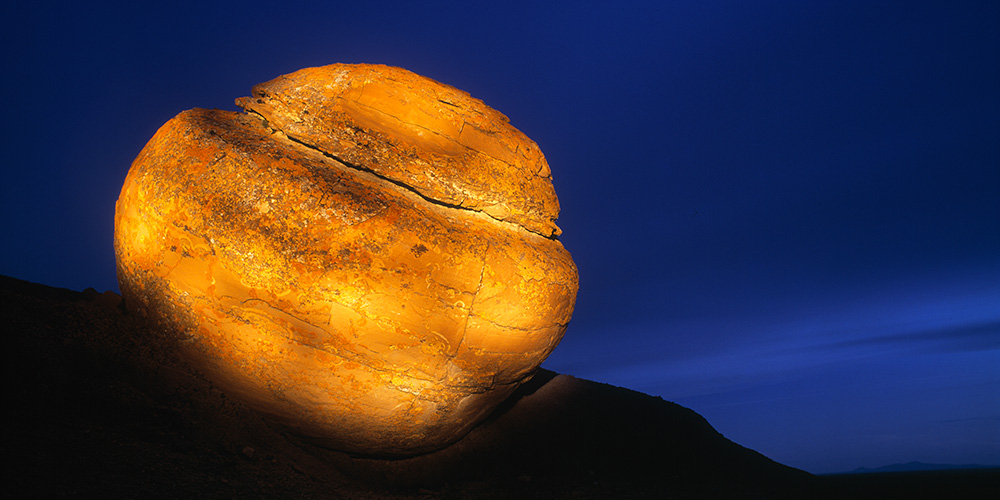 Large boulder lit by a flashlight against dusk sky