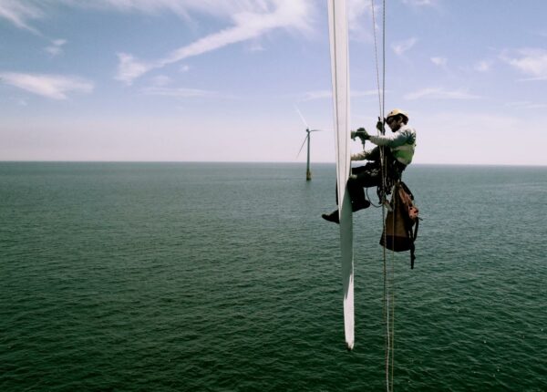 A rope access blade repair technician working on a wind turbine suspended above the ocean 
