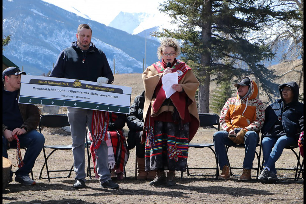 The new sign design being held while Amber Boyd (right) speaks at Cascade Ponds to mark the launch of the sign initiative  Jessica Lee  Rocky Mountain Outlook