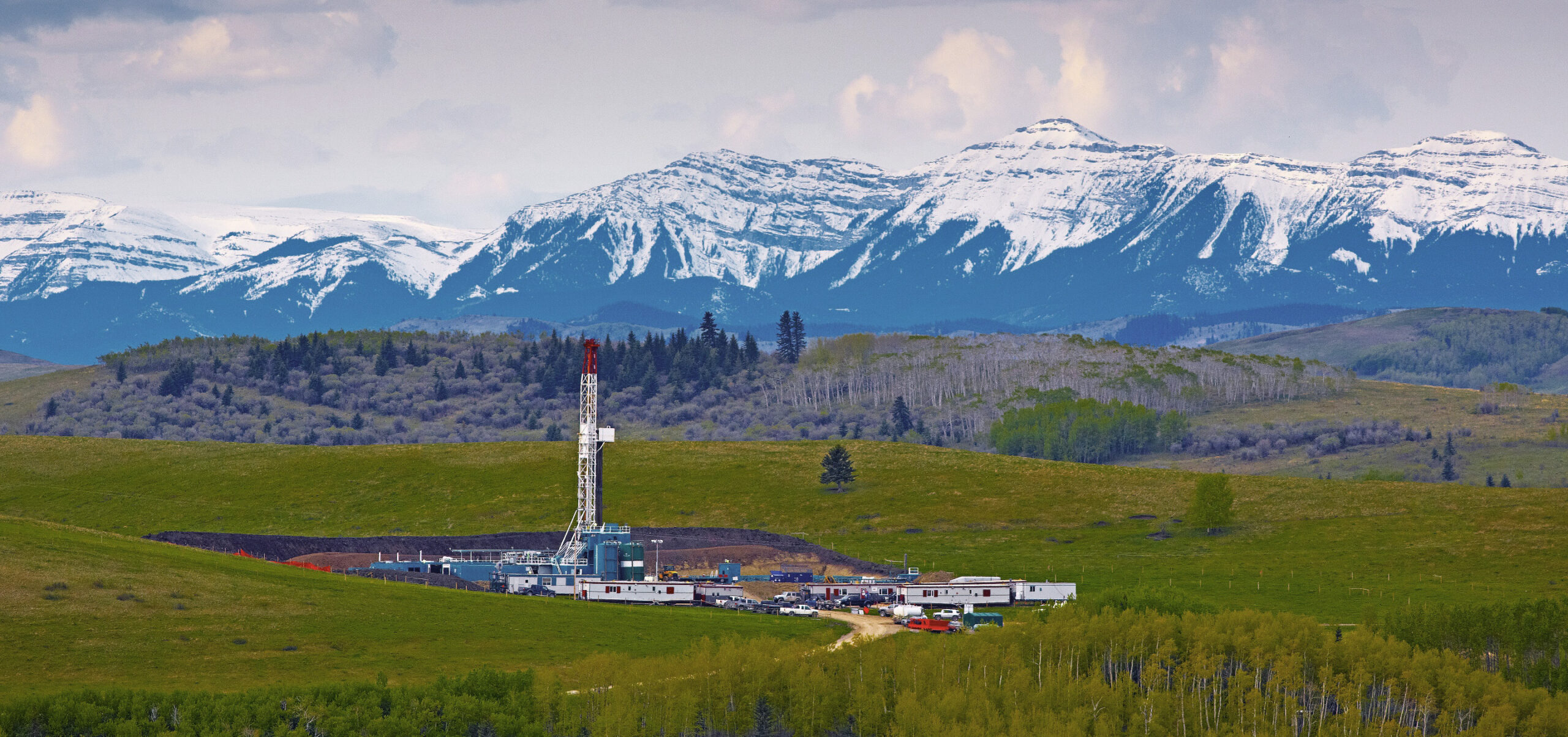 Photo of an oil rig in the foothills of southern Alberta with mountain peaks in the background
